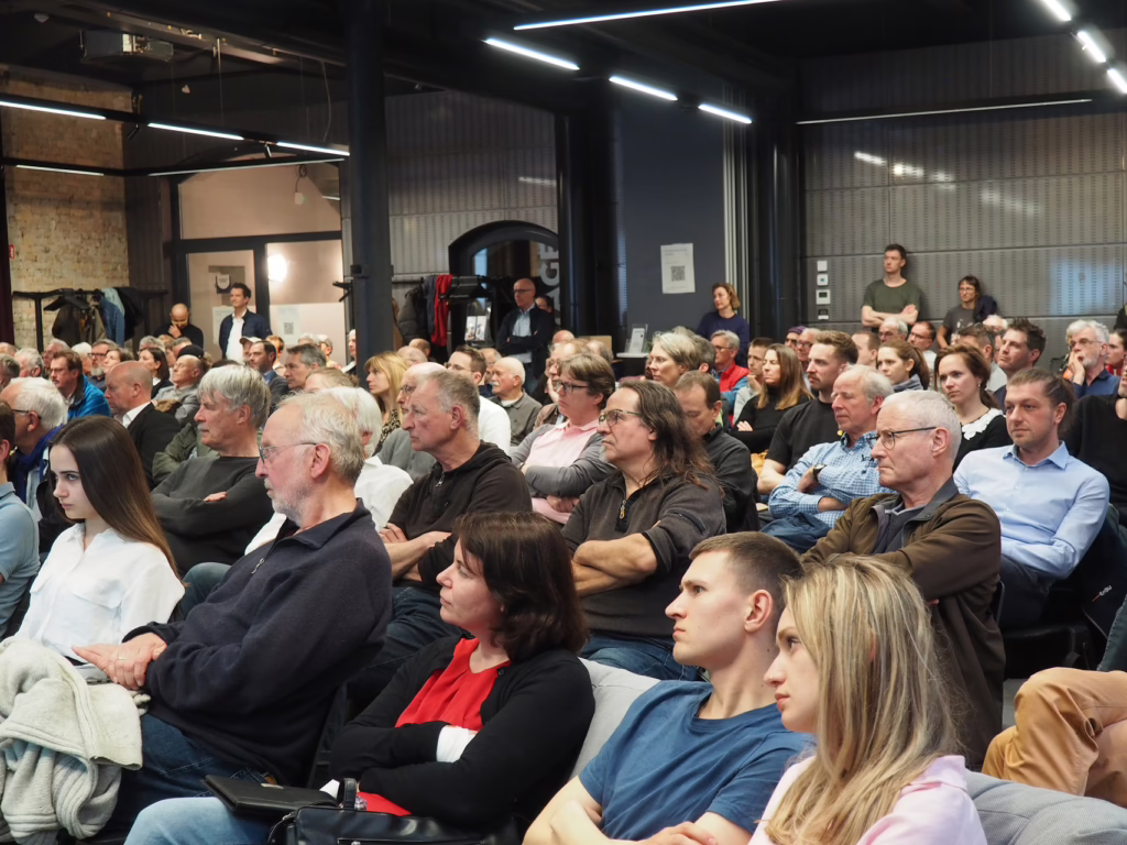 Das Publikumg des Wasserstoff Vortrags schaut gespannt an die Leinwand, auf der die Präsentation zu sehen ist. 