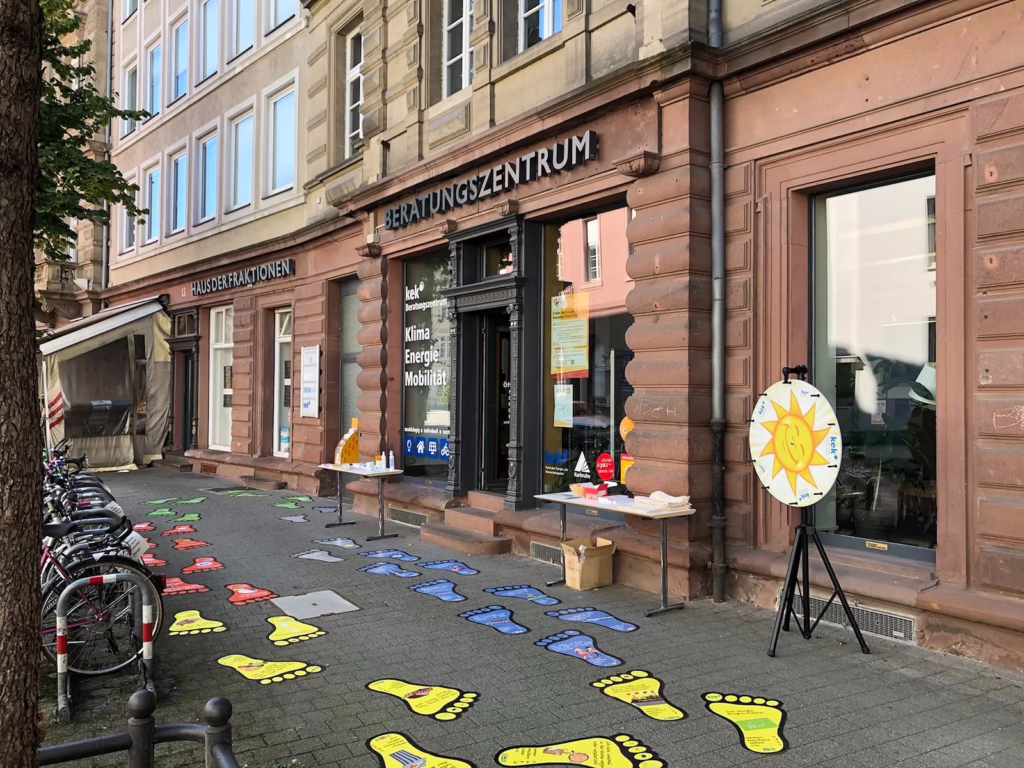 Das Beratungszetnrum ist von außen zu sehen. Davor sind Fußabdrücke auf dem Boden verteilt und ein Glücksrad ist aufgebaut.