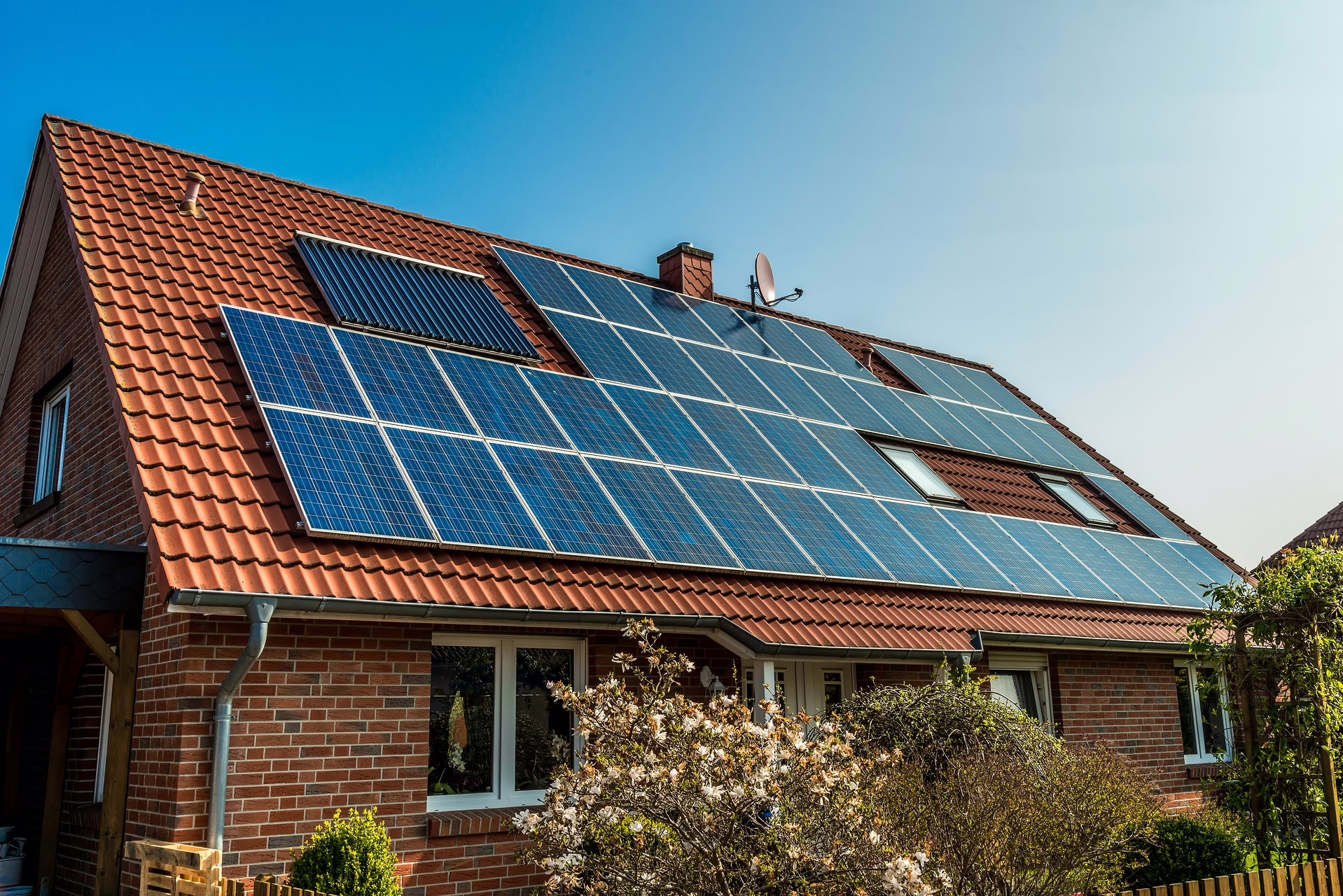 Im Beitrag geht es um das Solarspitzengesetz. Ein Einfamilienhaus mit großer Dachfläche ist mit Photovoltaikanlagen bestückt. Vor dem Haus ist ein kleiner Garten zu sehen.