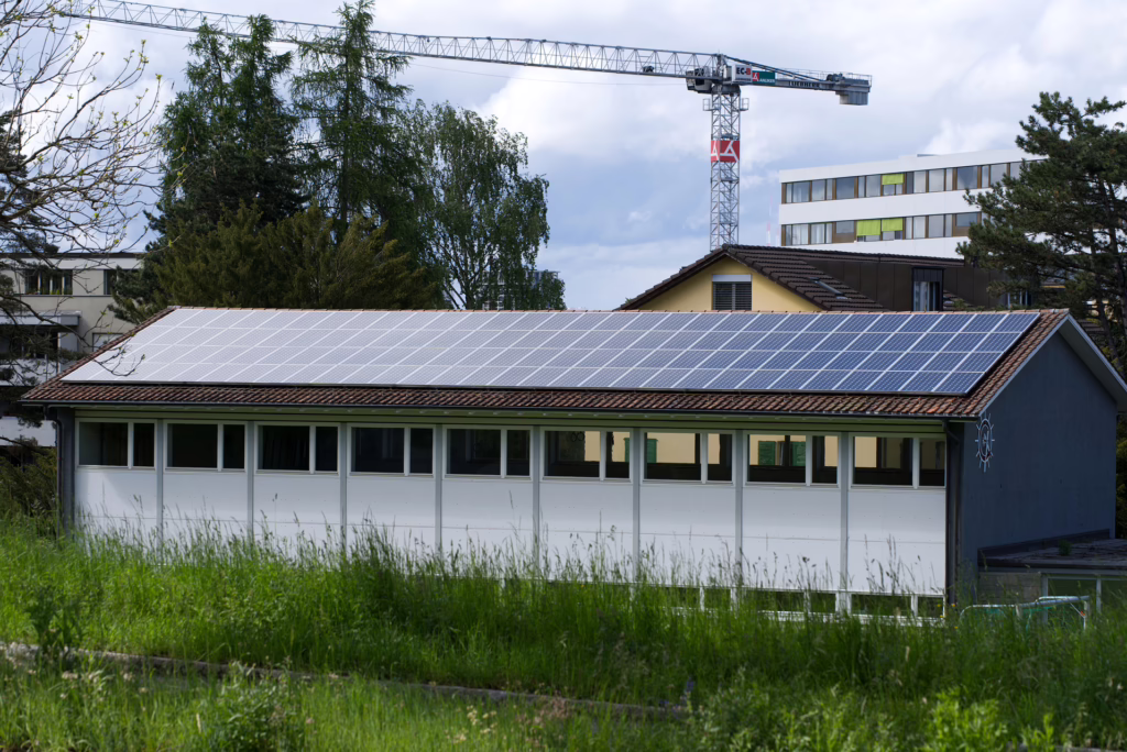 Auf dem Bild ist ein längliches Gebäude zu sehen, das von einem Verein sein könnte. Das Dach ist mit Photovoltaik ausgestattet.